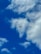 A commercial airplane flying high in the sky surrounded by scattered white clouds against a vibrant blue backdrop.