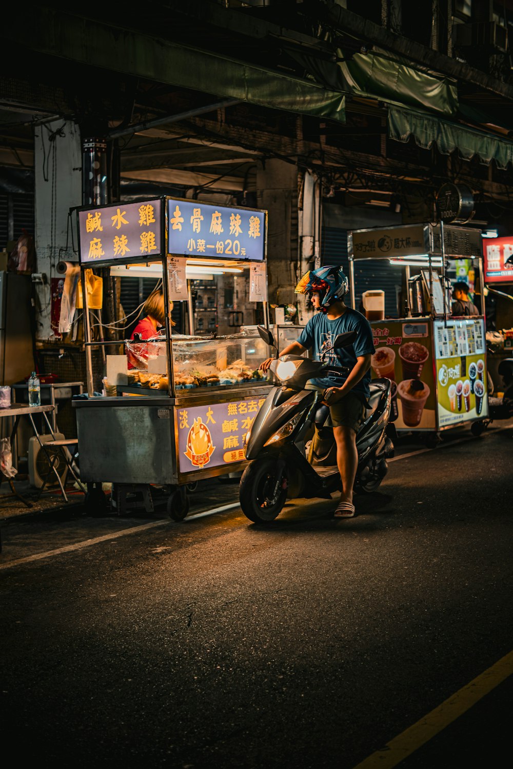 a man riding a motorcycle down a street next to a food stand