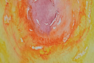 An abstract watercolor painting featuring a swirling pattern of vibrant colors. The central area is dominated by shades of pink and purple, gradually transitioning into bright orange and yellow hues. The texture suggests a mix of smooth and rough brushwork with visible paint strokes.