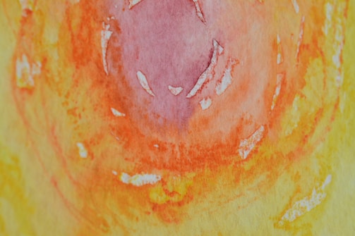 An abstract watercolor painting featuring a swirling pattern of vibrant colors. The central area is dominated by shades of pink and purple, gradually transitioning into bright orange and yellow hues. The texture suggests a mix of smooth and rough brushwork with visible paint strokes.