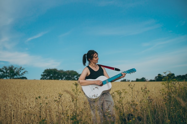 a woman standing in a field holding a guitar