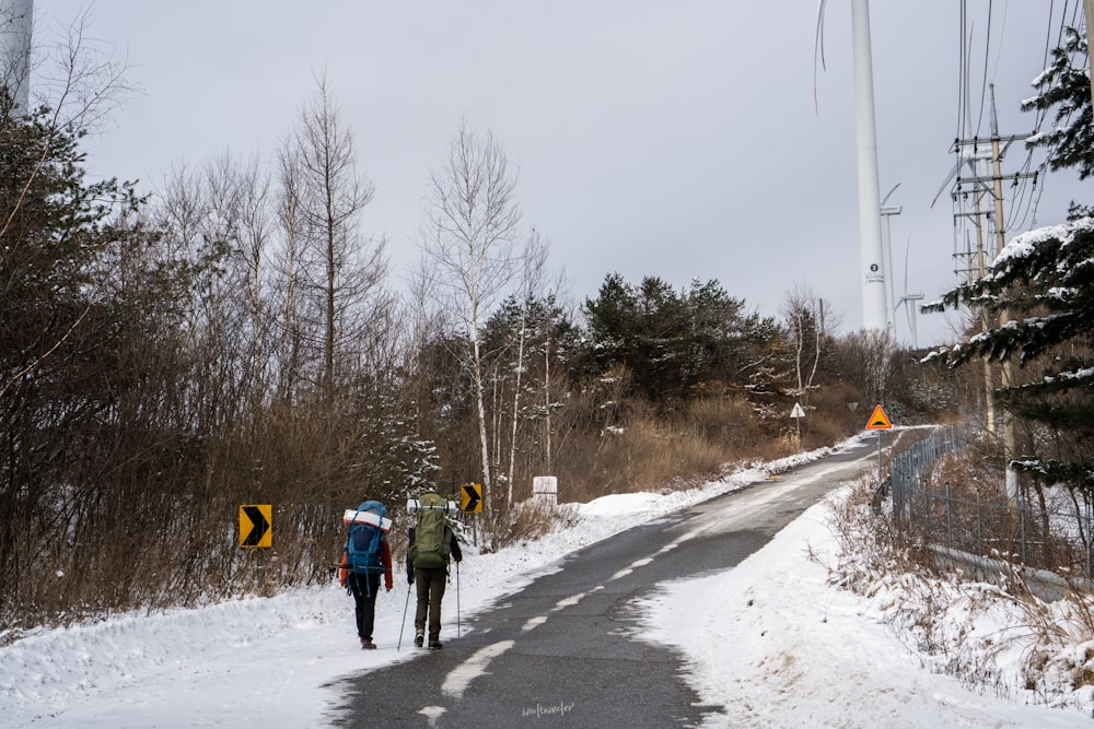 a couple of people walking down a snow covered road