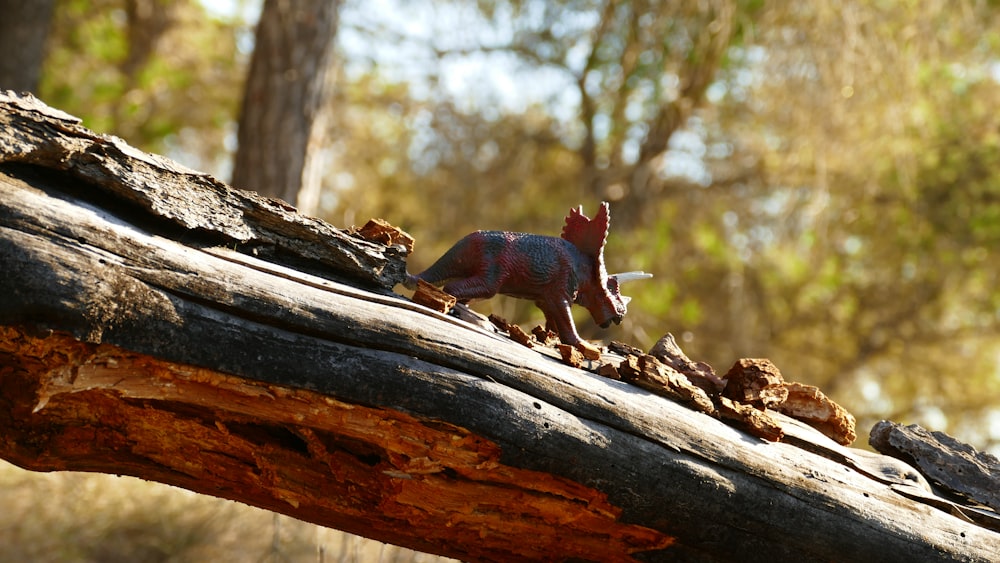 a toy dinosaur on a log in the woods