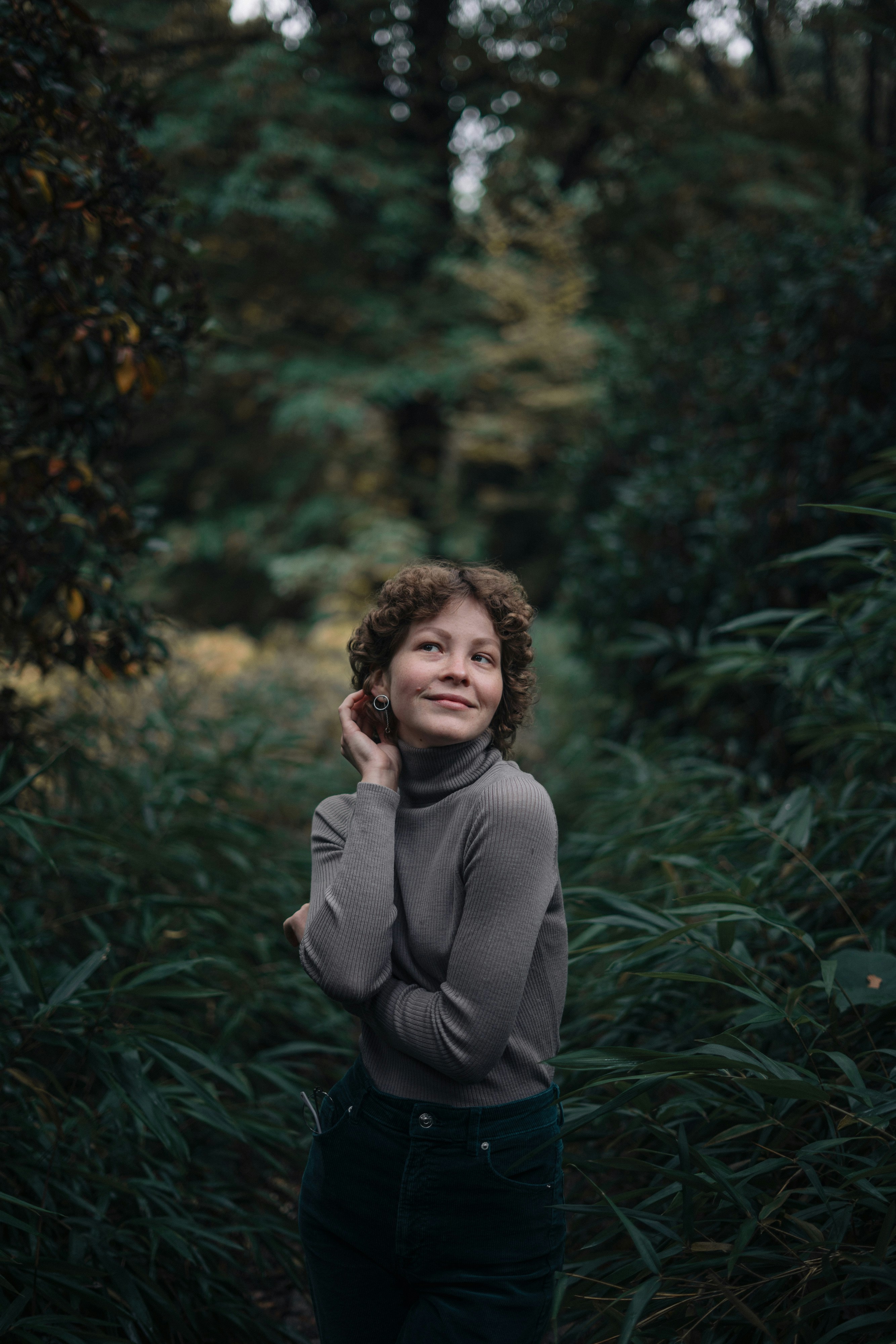 a woman standing in a forest with her hands on her head