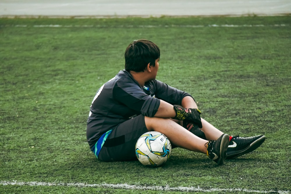 축구공을 들고 바닥에 앉아 있는 어린 소년