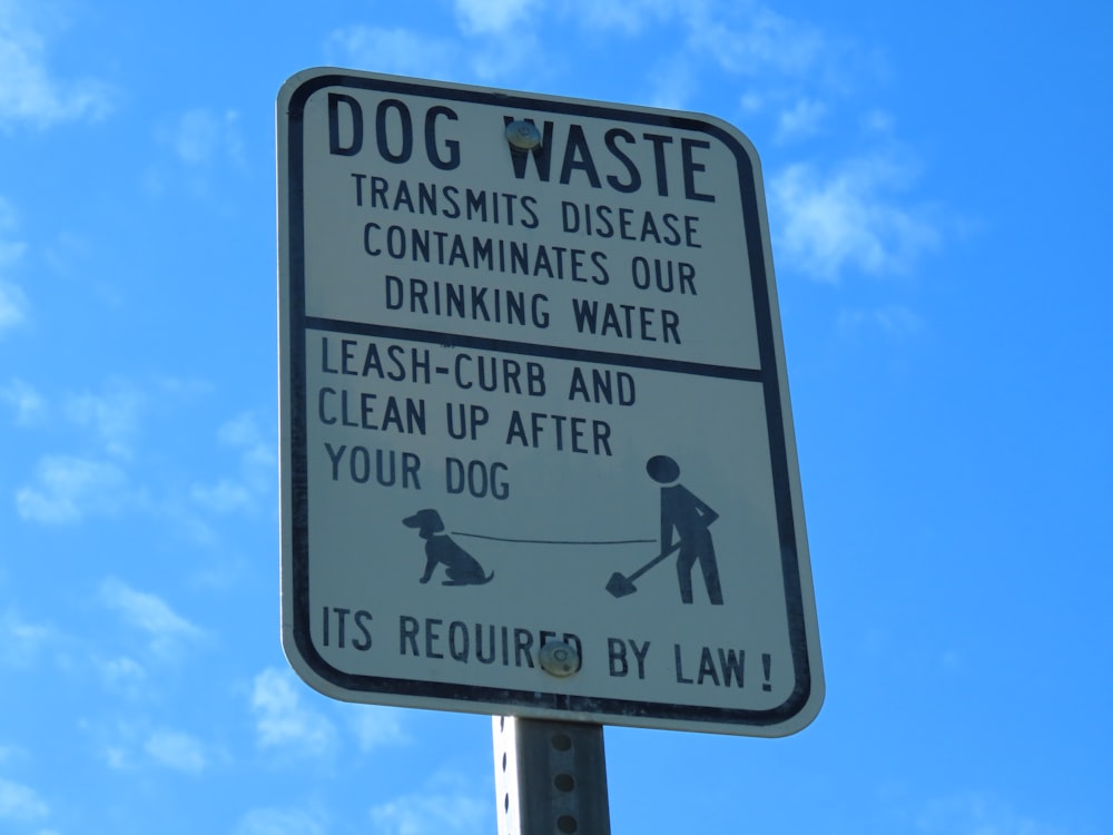 a dog waste sign on a pole with a blue sky in the background