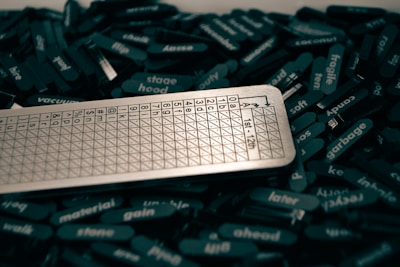 A collection of black tiles with white text scattered around, featuring various words. A metallic scoring sheet or board with a grid and numbers is positioned prominently among them.