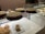 A bakery display case containing several pastries and cakes. Three large cakes with lattice tops are prominently featured on a glass shelf, with one cake partially sliced. Below on a white plate, there are cream-filled pastries and a croissant.