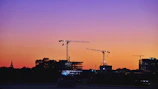 Sunset silhouette of construction cranes against a vibrant sky.