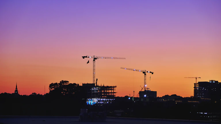 Sunset silhouette of construction cranes against a vibrant sky.