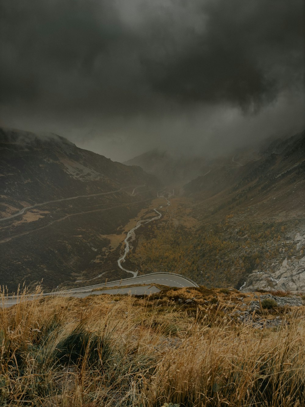 a winding road in the mountains under a cloudy sky