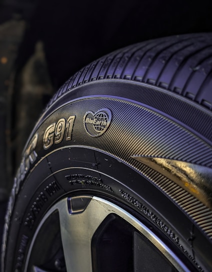 A close-up view of a car tire featuring detailed tread patterns and branding information such as text and logos. The tire surface appears glossy, with the focus on the sidewall markings and tread design.