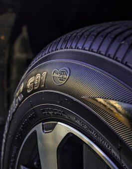 A close-up view of a car tire featuring detailed tread patterns and branding information such as text and logos. The tire surface appears glossy, with the focus on the sidewall markings and tread design.