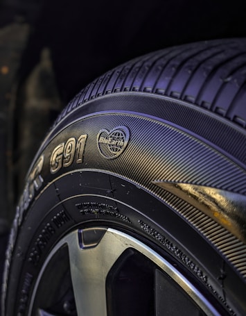 A close-up view of a car tire featuring detailed tread patterns and branding information such as text and logos. The tire surface appears glossy, with the focus on the sidewall markings and tread design.