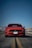A smiling man standing next to a sleek red Mustang convertible on a sunny Texas highway.