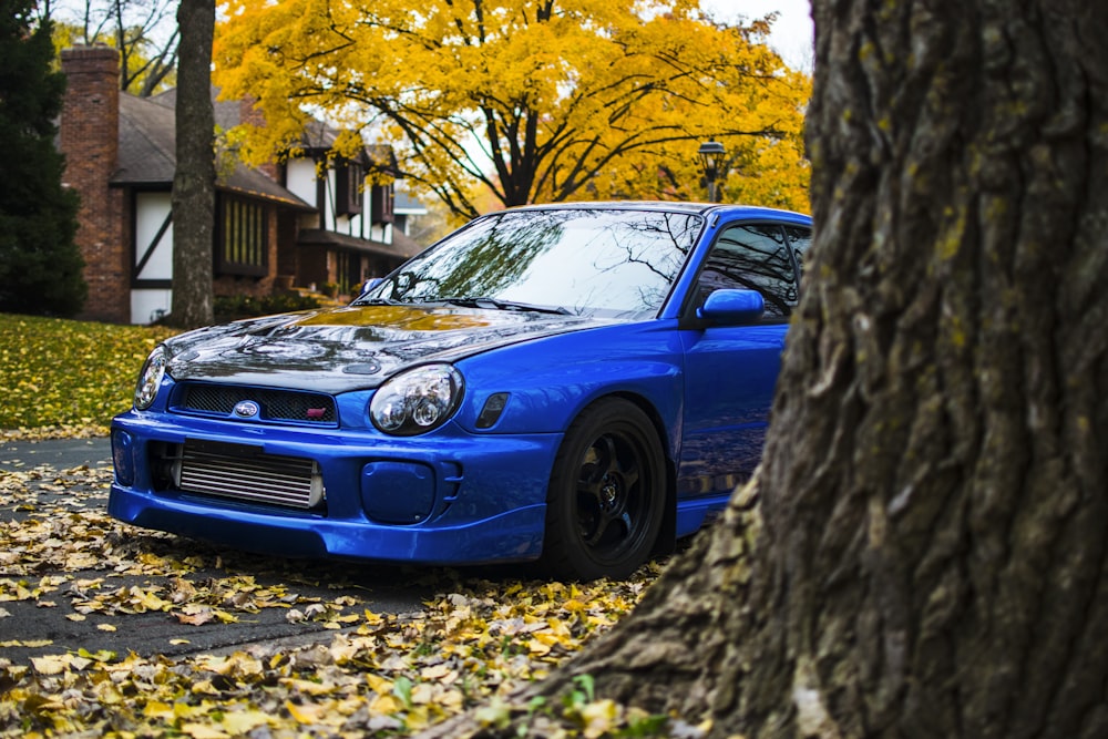 a blue car parked in front of a tree