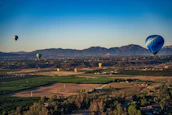 Smiling tourists enjoying a peaceful hot air balloon ride above a patchwork of farmland.