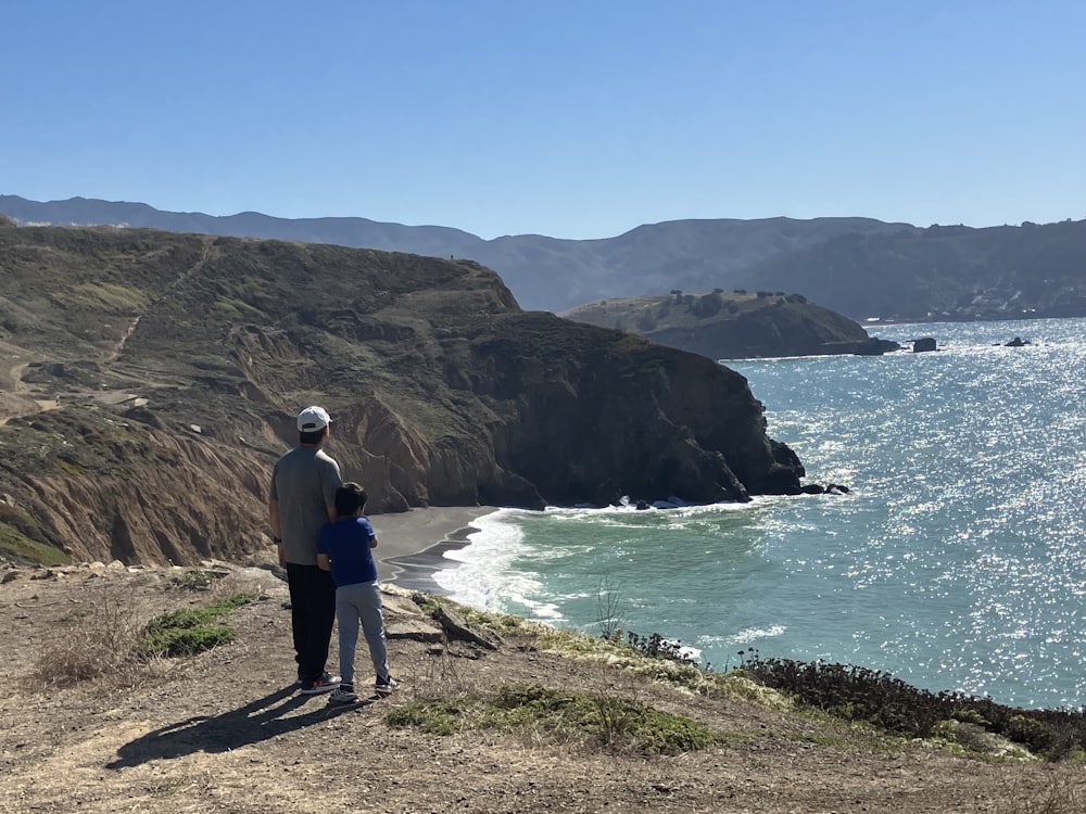 a man and a child standing on a cliff overlooking the ocean