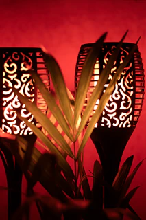 A close-up of a brass Moroccan lantern glowing warmly against a backdrop of terracotta walls and emerald green cushions.