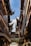 Traditional Chinese architecture featuring intricate, upward-curving tiled roofs framed against a clear blue sky. Wooden structures with detailed carvings and hanging lanterns adorn the narrow alleyway.