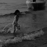 Children laughing and splashing in shallow waves near the beach, with colorful umbrellas dotting the sand.