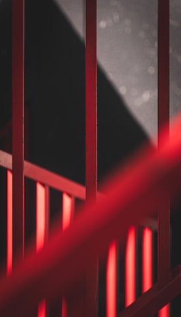 Red metal railings intersecting with dramatic shadows and contrasting light, creating an abstract and geometric composition.