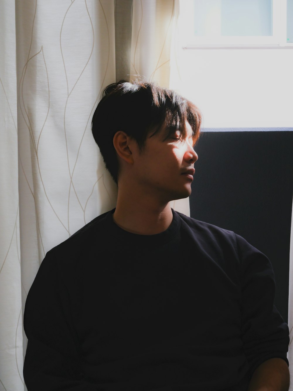 a young man sitting in front of a window