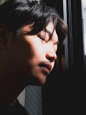 a man with his eyes closed looking out a window