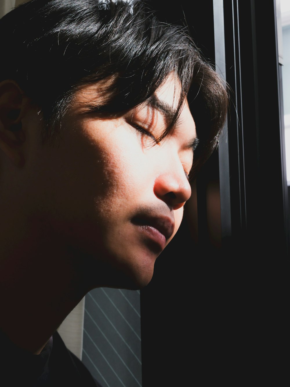 a man with his eyes closed looking out a window