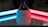 A security camera with a dome-shaped glass cover is placed on a reflective surface. The background features two neon lights, one blue on the left and one red on the right, casting colorful reflections.
