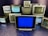 A group of old television sets stacked together with some screens showing static and others off. In the center, one television has a blue screen.