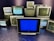 A group of old television sets stacked together with some screens showing static and others off. In the center, one television has a blue screen.