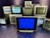 A group of old television sets stacked together with some screens showing static and others off. In the center, one television has a blue screen.