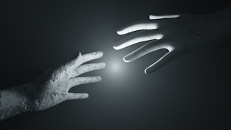 A stone-textured human hand reaches out towards a robotic hand with an illuminated point between them, set against a dark and minimalistic background.