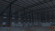 A large, open industrial warehouse interior with a high ceiling and metal beams. Several stacks of large white rolls are placed throughout the area. The space is well-lit by natural light filtering in from rectangular windows along the walls.