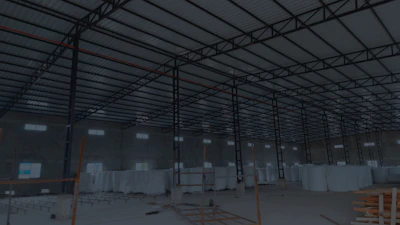 A large, open industrial warehouse interior with a high ceiling and metal beams. Several stacks of large white rolls are placed throughout the area. The space is well-lit by natural light filtering in from rectangular windows along the walls.