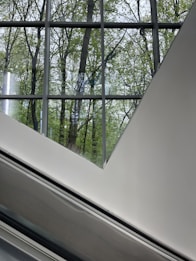 Large glass windows provide a view of green trees framed by a geometric, modern architecture with clean lines and smooth surfaces.