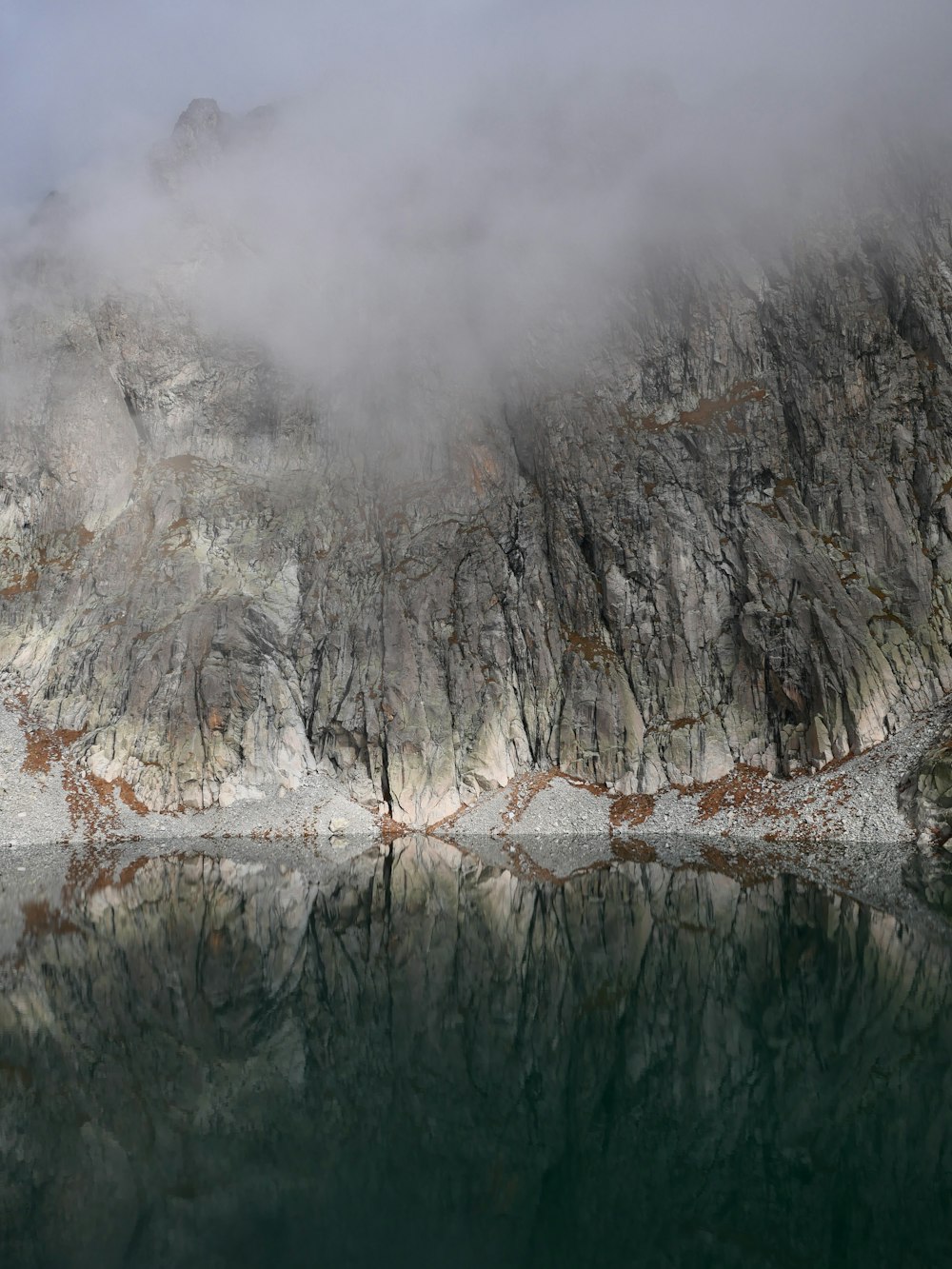 una montaña cubierta de niebla y nubes junto a un cuerpo de agua