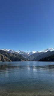 A tranquil lake in Lucerne reflecting the surrounding snow-capped mountains under a clear blue sky.