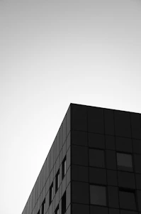 A minimal black-and-white photograph of a modern architectural corner with sharp shadows.