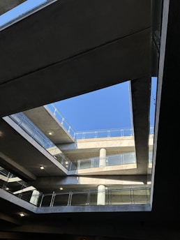 Multiple levels of a concrete structure are seen with railings and a clear view of the sky above. The setting suggests an architectural design with open spaces and lines intersecting at various angles.