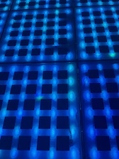 A glowing neon checkerboard pattern with bright pink, blue, and green squares illuminating a dark background.
