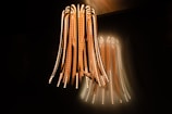 A unique and modern light fixture hangs from the ceiling, consisting of multiple long, flexible strips with embedded LED lights. The lights emit a warm glow against a dark background, creating an ambient atmosphere with the light reflecting on the wall.