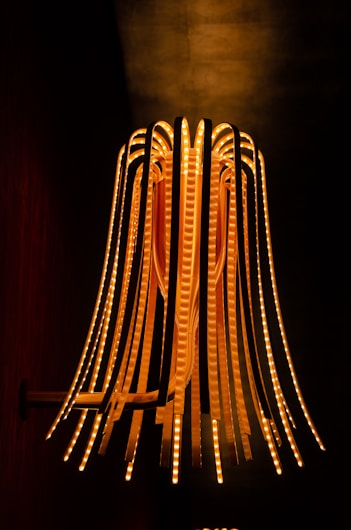 A decorative pendant light with multiple curved strips illuminated by warm LED lights, creating a visually striking and modern art piece against a dark background.