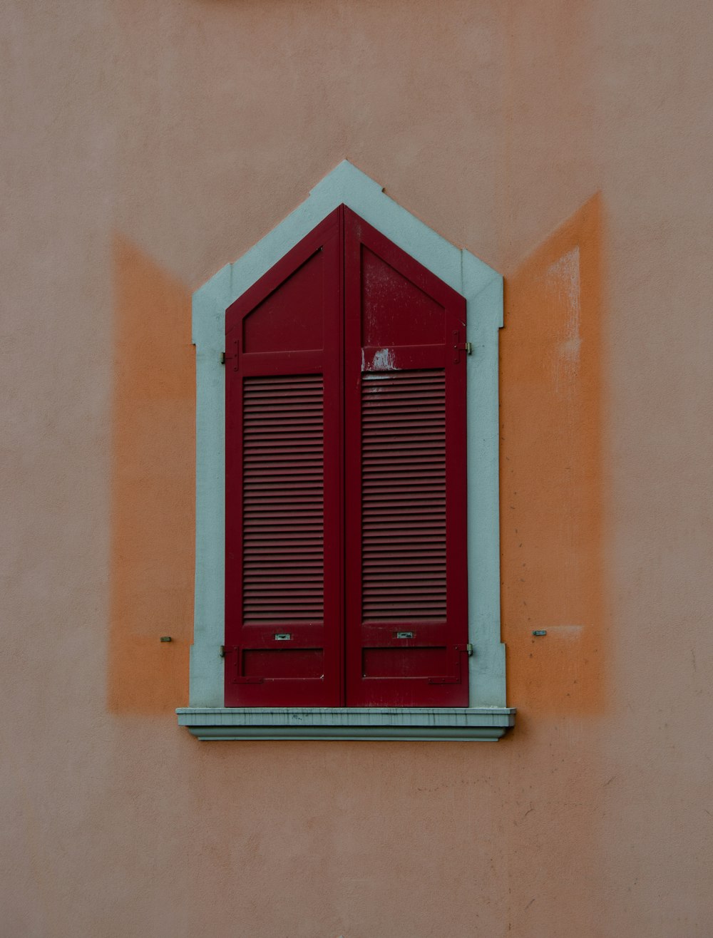 una ventana roja con persianas en una pared rosa