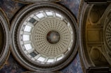An intricately designed dome with ornate patterns and detailed artwork. The circular pattern features layers of designs with a central circular mural surrounded by geometric shapes. Large windows encircle the dome, allowing natural light to illuminate the space. The architectural details include ornate moldings and decorative plasterwork.