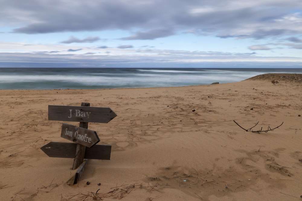 a wooden sign pointing to two different directions on a beach