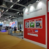 a red and white trade show booth with people standing around