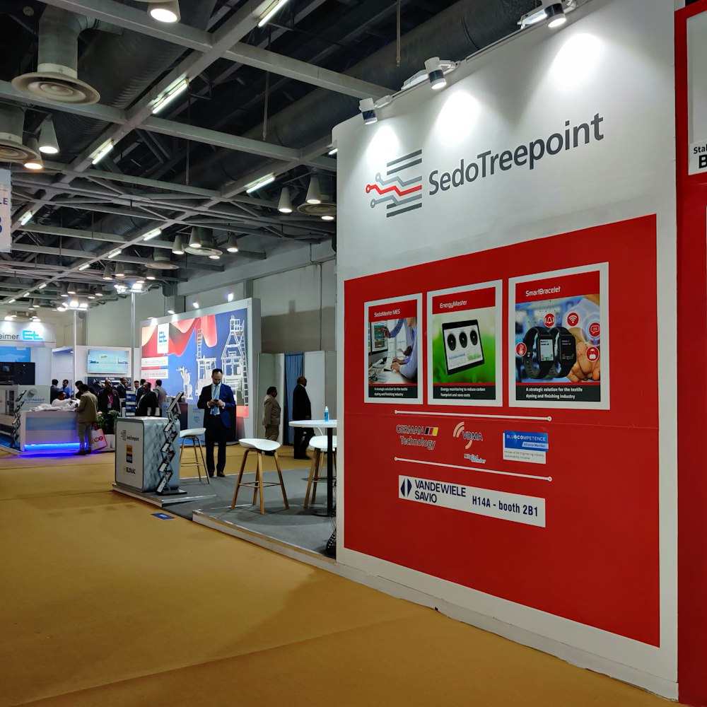 a red and white trade show booth with people standing around