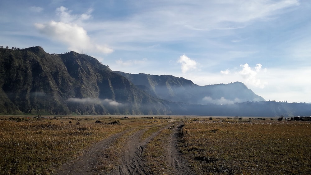 a dirt road in front of a mountain range